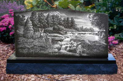 Granite monument with an etched scene of deer beside a river and pine trees