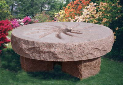 Round millstone table bench in red granite standing on cut stone legs in a garden